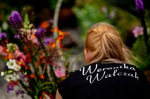 Weronika Walczak od tyłu przy kolorowych kwiatach, z imieniem i nazwiskiem na koszulce