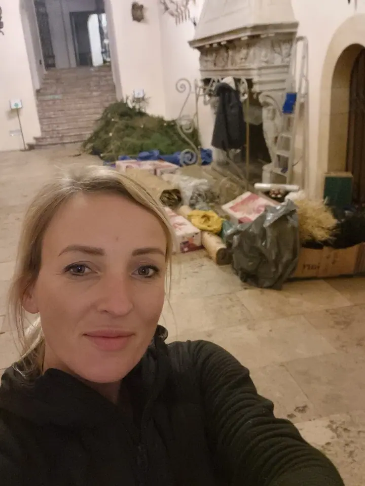 Weronika Walczak w sali z porożami jelenimi, za nią przywiezione gałęzie, choinki i materiały do dekoracji