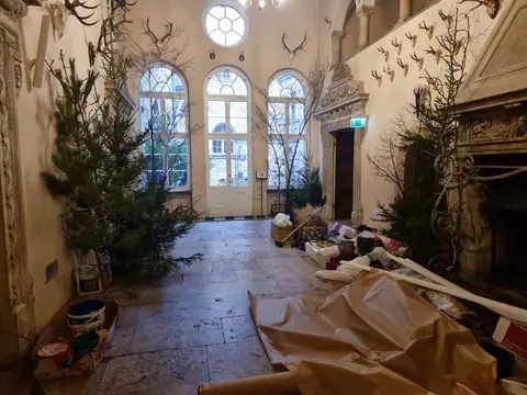 Sala z porożami na ścianach w trakcie aranżacji: ustawione choinki, gałęzie i rozłożony szary papier